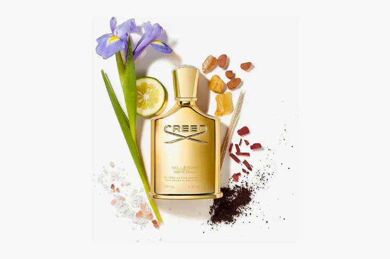 Frasco dourado do perfume Creed Millésime Impérial Eau de Parfum 100ml com flores ao fundo