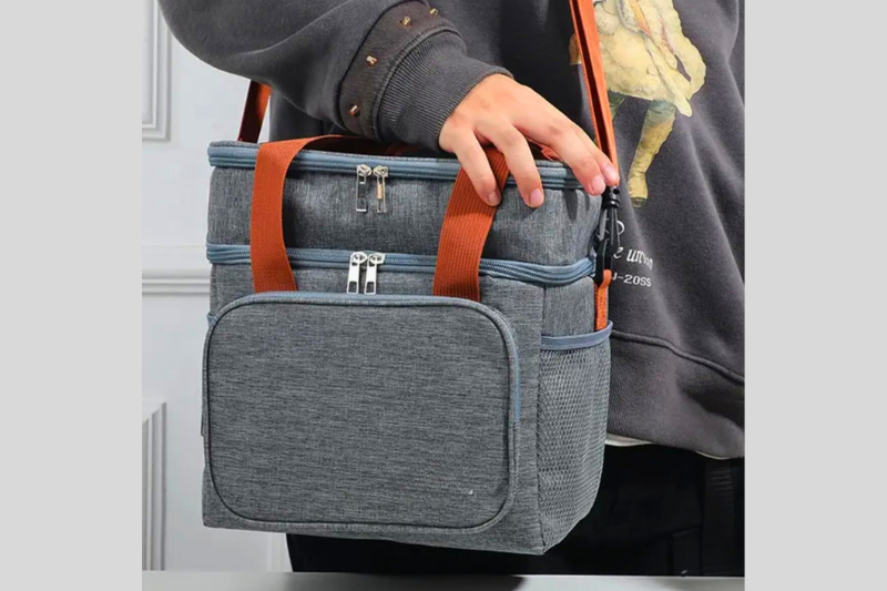 Pessoa segurando uma bolsa térmica cinza pelo cabo reforçado.