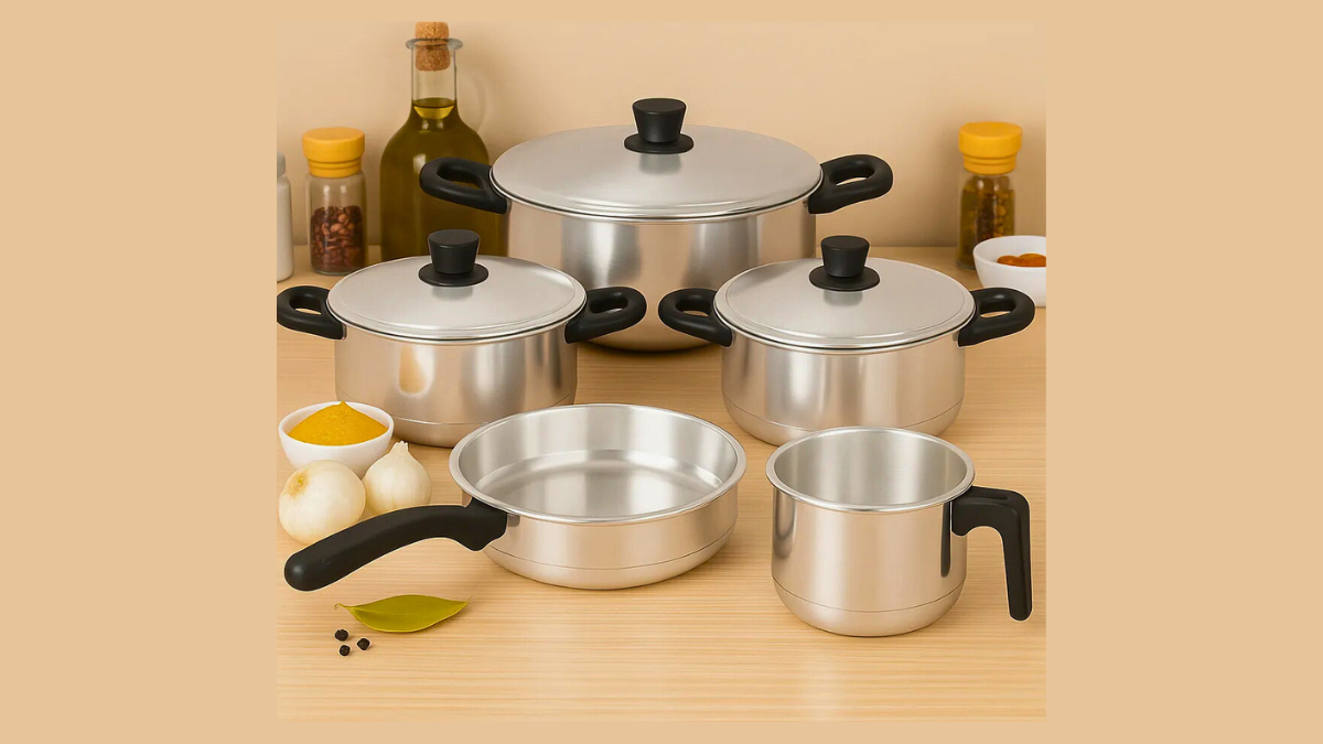 Conjunto de panelas de cozinha em inox organizadas sobre a bancada ao lado de alimentos e utensílios.