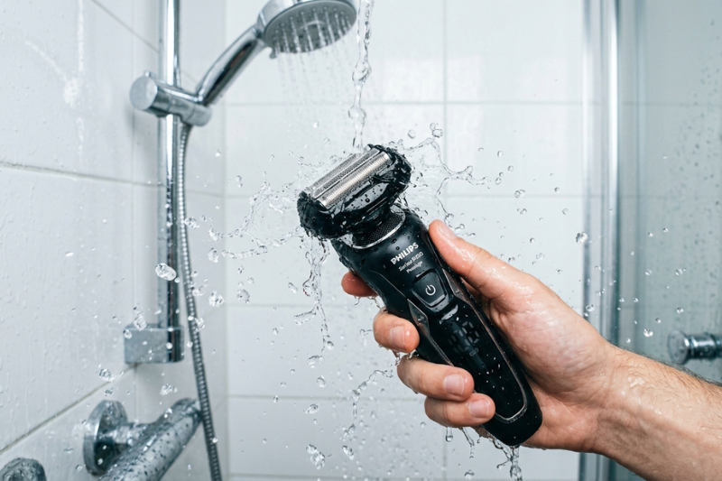 Barbeador elétrico Kemei KM-2024 sendo usado debaixo do chuveiro para demonstrar sua praticidade e resistência à água.